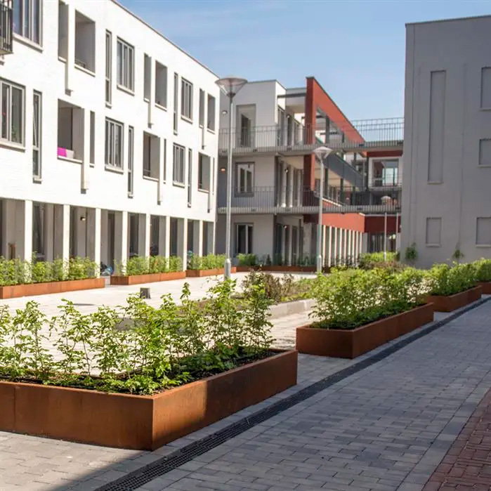 Moderni asuinalue, jossa istutusaltaat on rajattu kapeilla suorilla corten-teräksisillä reunatuilla.