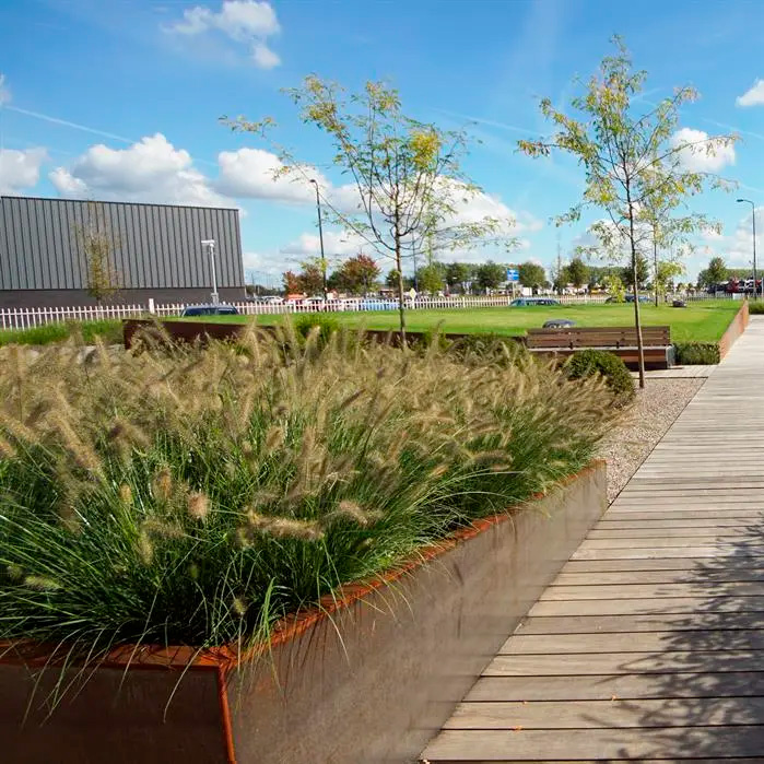 Maisemapenkki ja istutusalue, jossa kapea corten-teräksinen ulkokulmareunatuki puisen kävelytien vieressä.